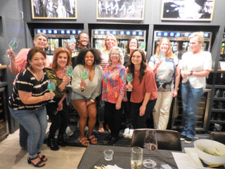 Group of people posing together in a casual setting with drinks and snacks.